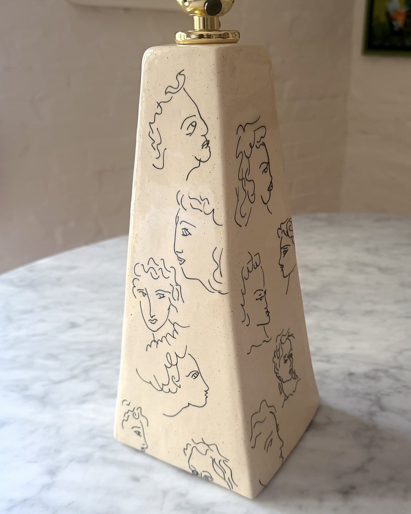 A tall, tapered ceramic lamp base covered in line-drawn faces.