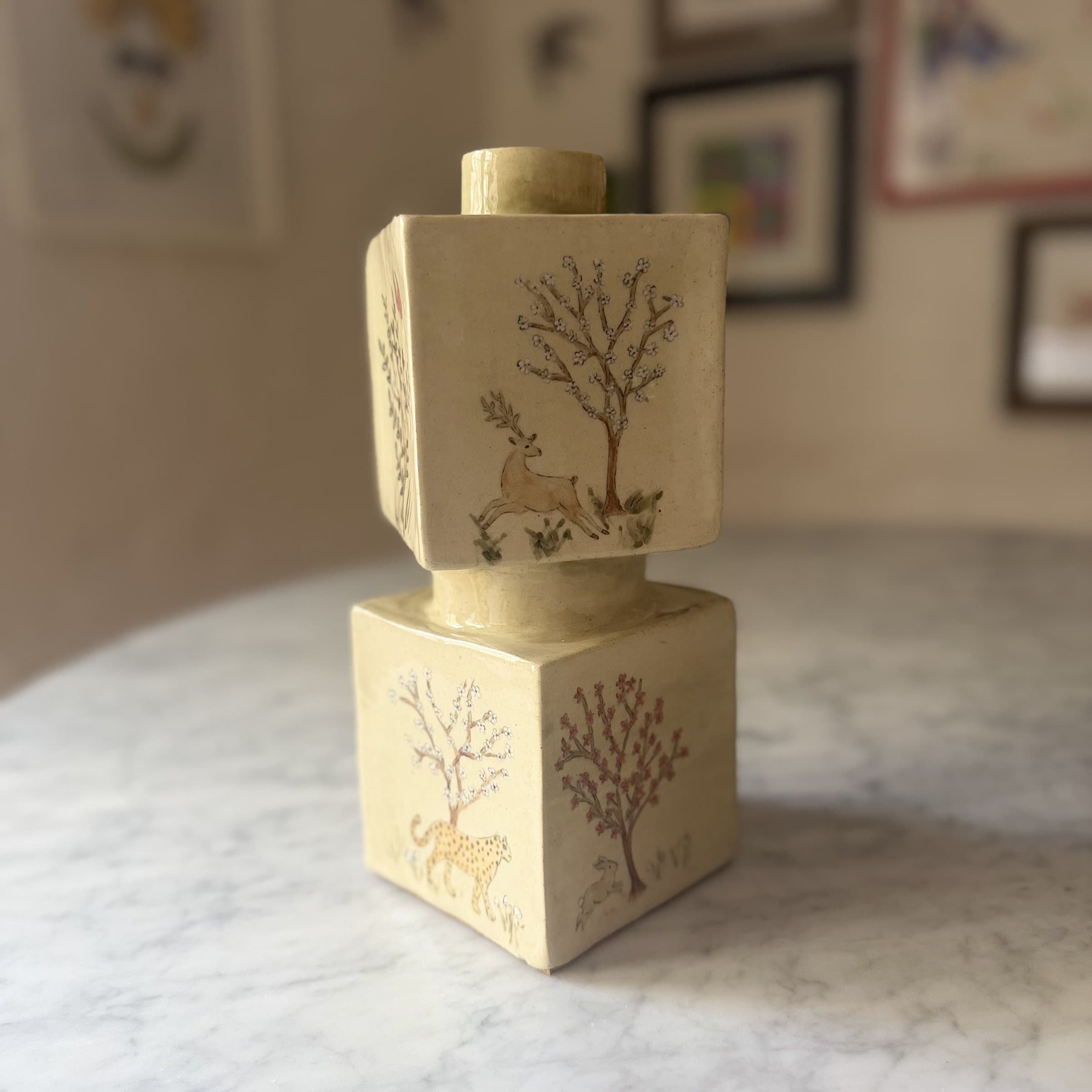 A stacked cube ceramic lamp base painted with trees and animals on each side.