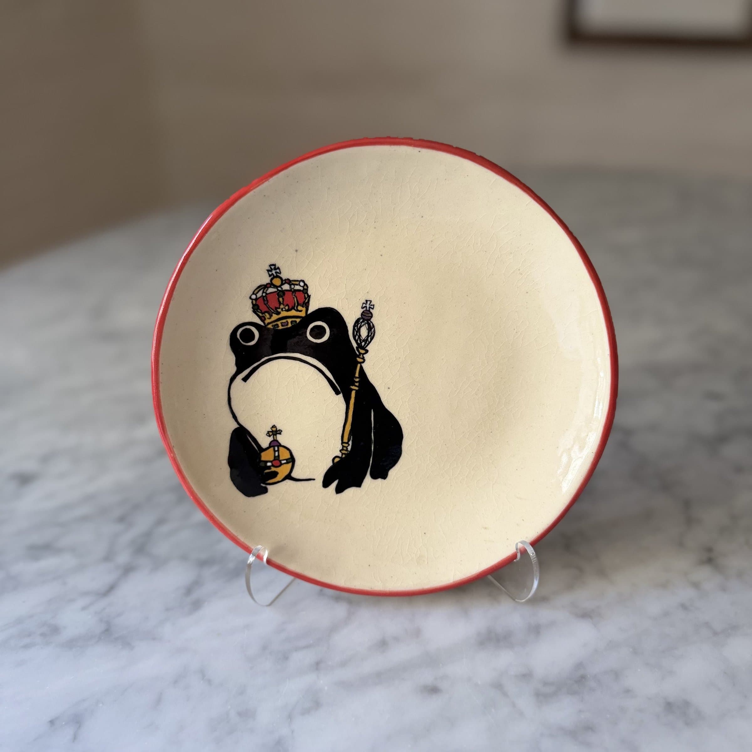 A plate painted with a frog wearing a royal crown and holding a scepter and orb.