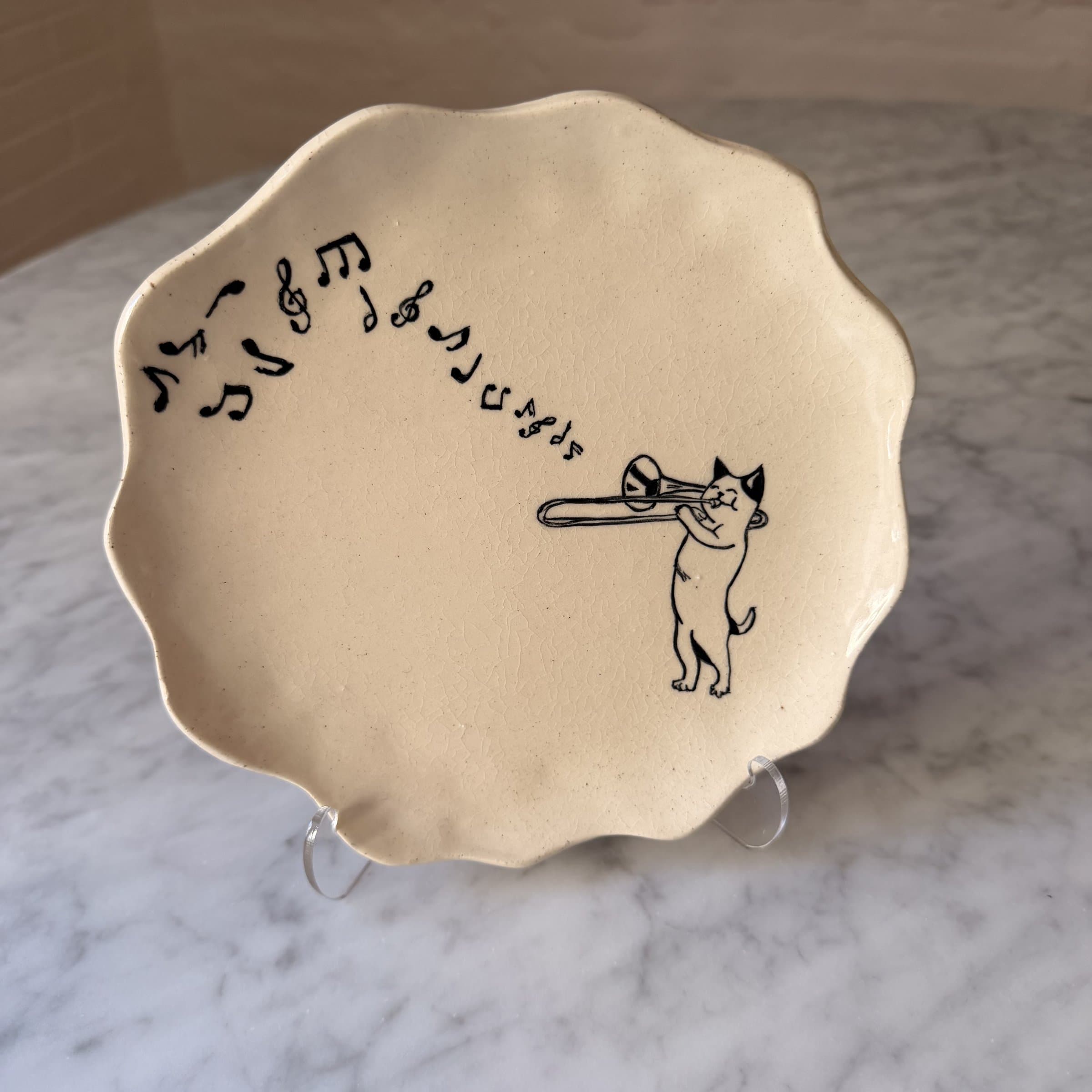 A scalloped plate painted with a cat playing the trombone, music notes rising.