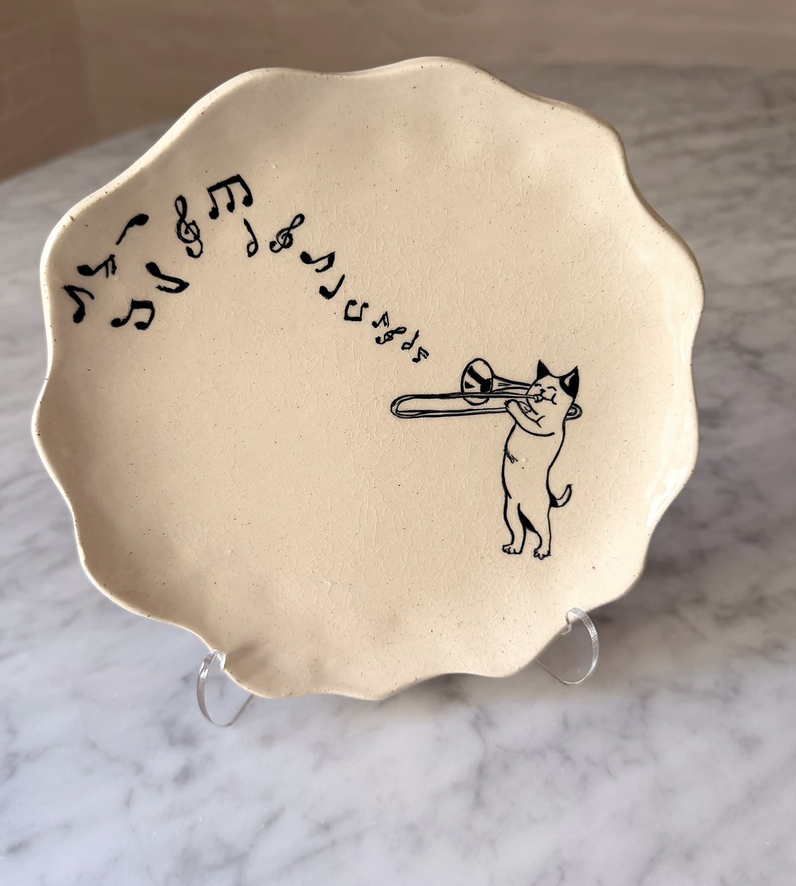 A scalloped plate drawn with a cat playing trombone, notes trailing across the plate.