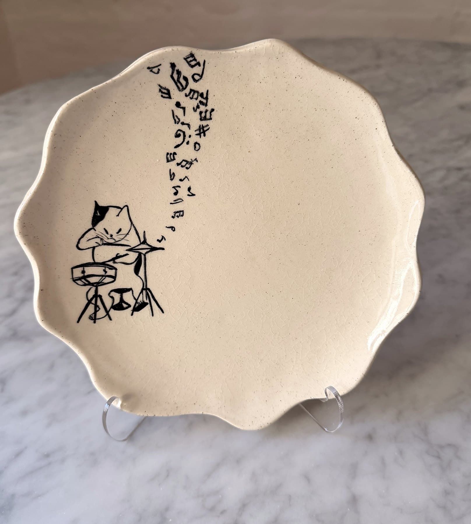 A scalloped plate drawn with a cat playing drums, notes flying up the plate.