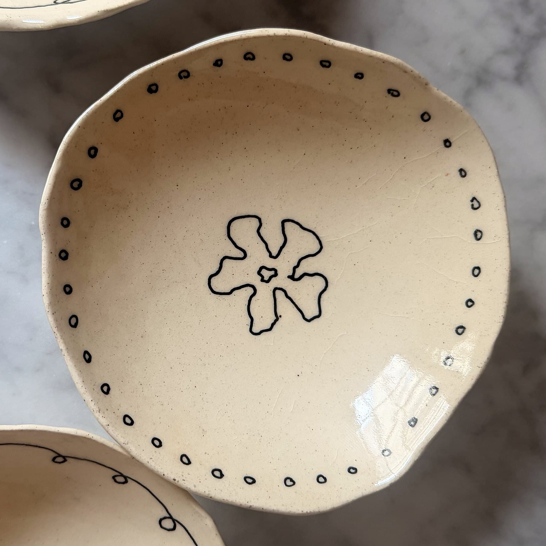 A hand-built cream bowl with a dotted border and a single flower.