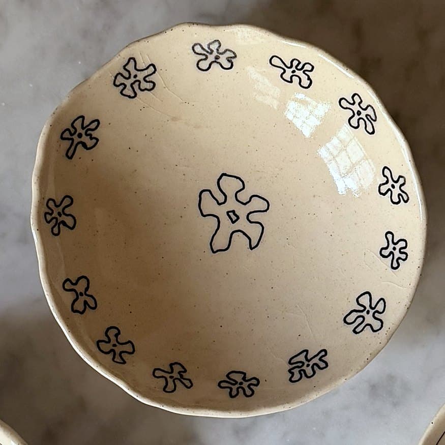 A scalloped cream bowl ringed with small black flowers around a larger one.