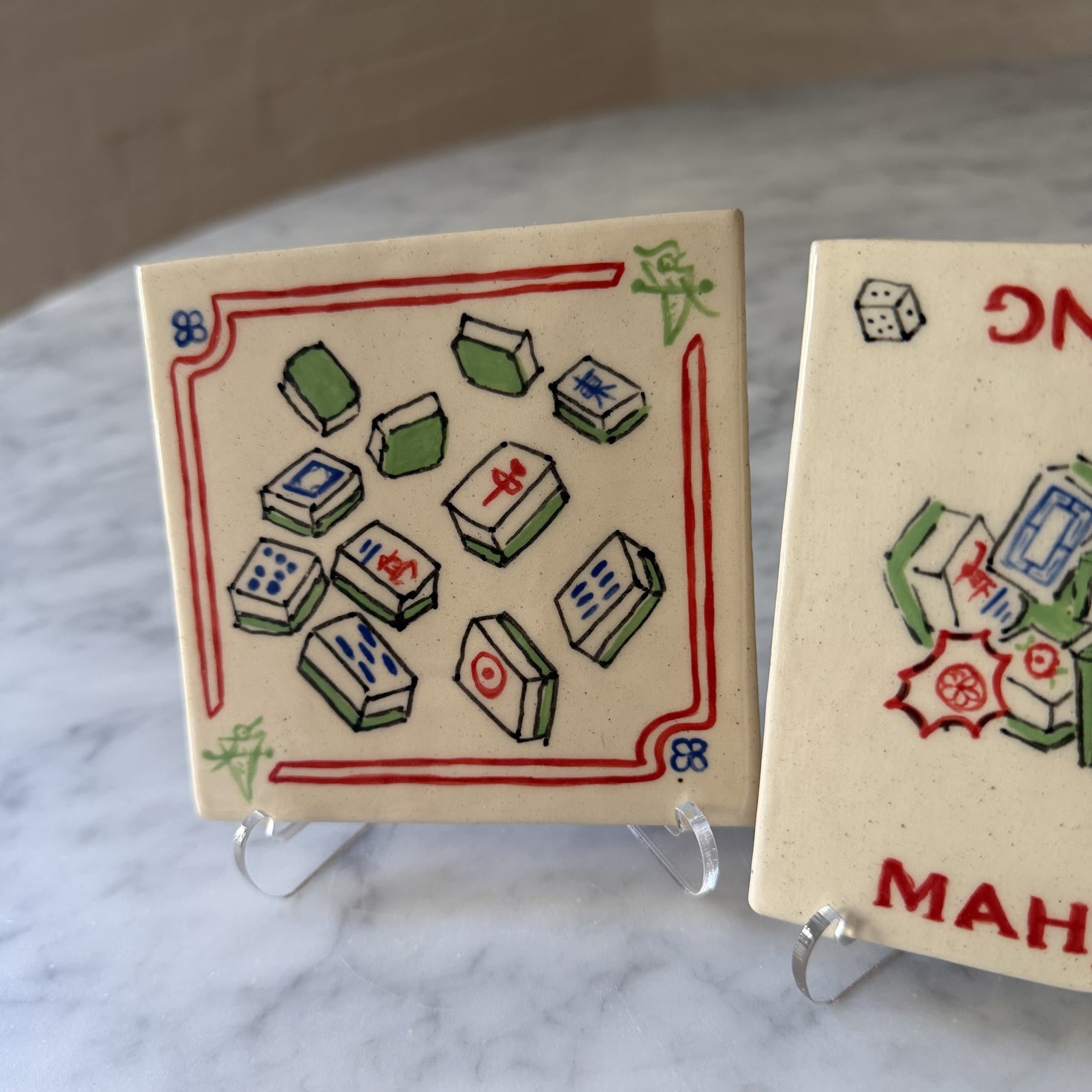 A hand-painted tile of mahjong tiles scattered in mid-game, with green and red detailing.