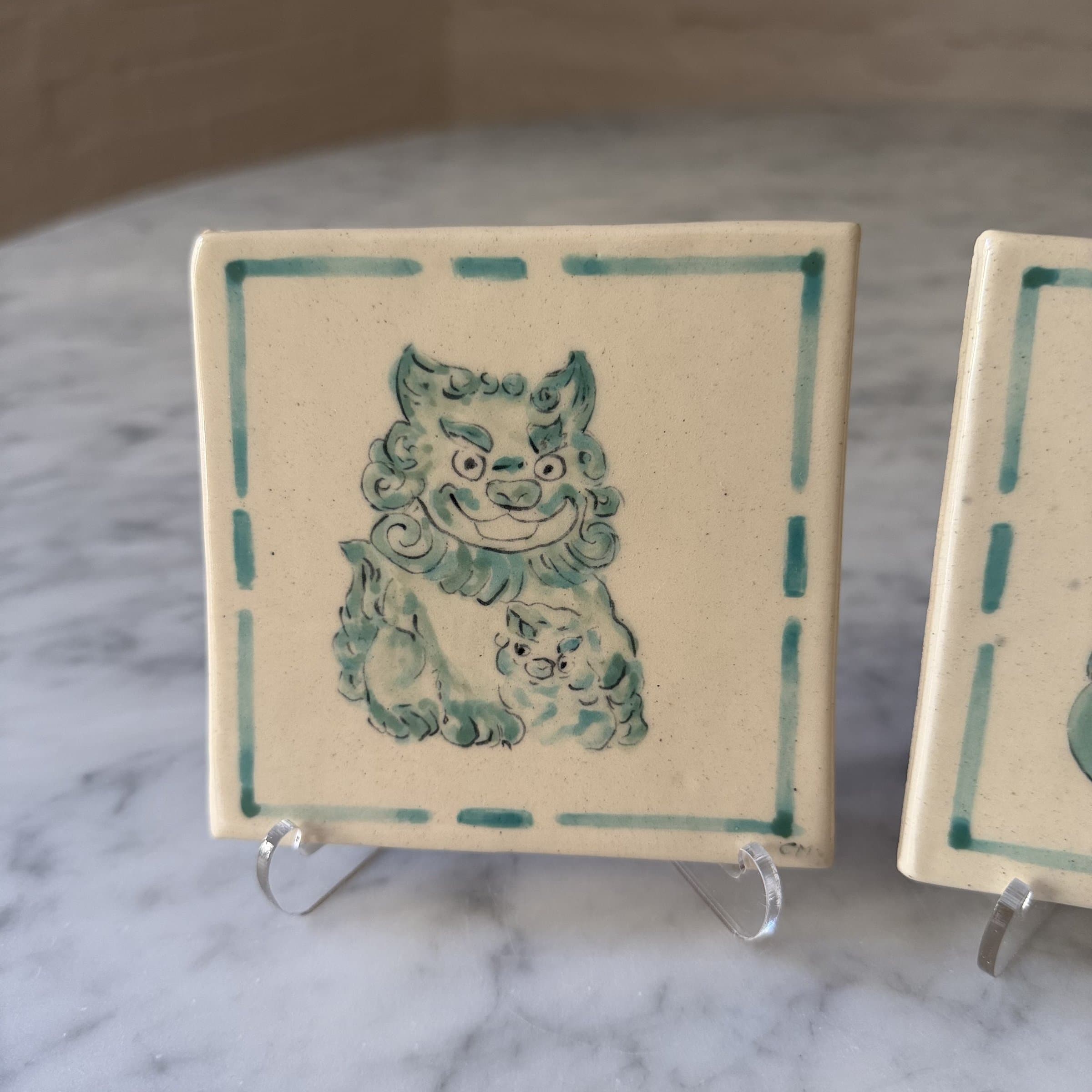 A hand-painted tile of a smiling green foo dog with its cub.