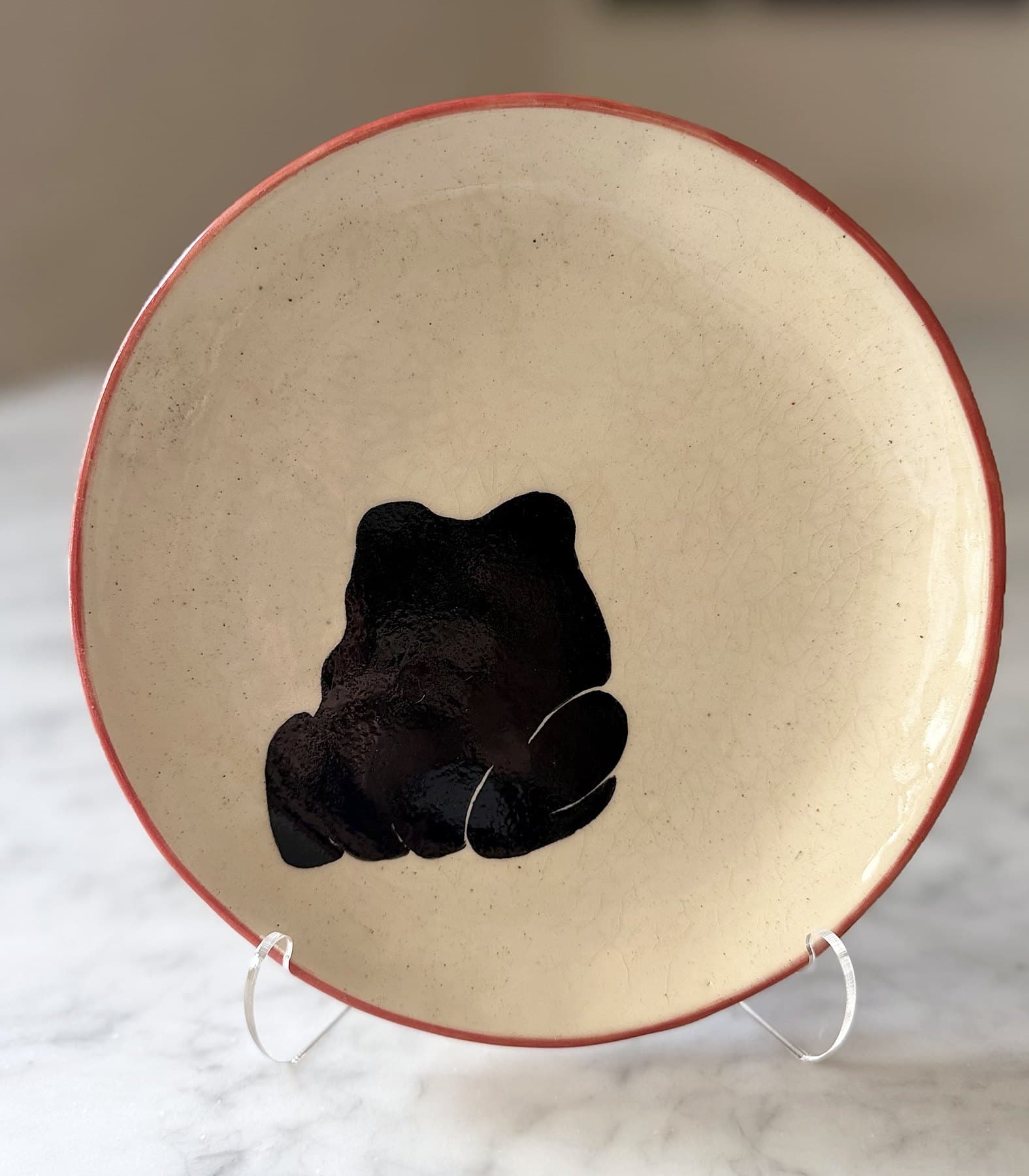 A red-rimmed plate painted with a black frog seen from behind.